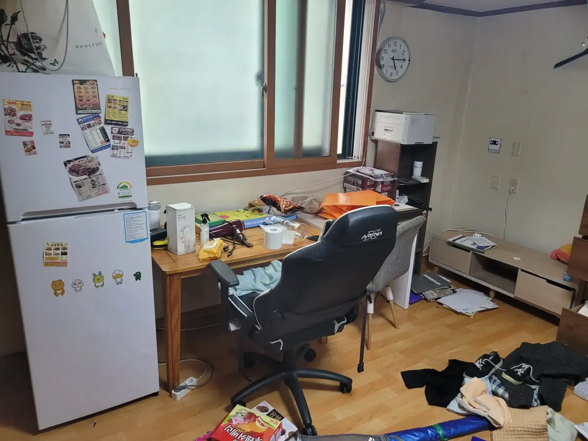 가구정리 전 책상과 사무용 의자, 냉장고, TV장이 놓인 원룸 창가