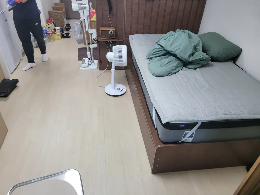 서랍형 수납 침대와 선풍기가 놓인 좁고 긴 원룸 내부